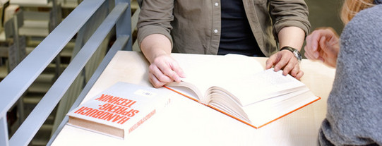 Zwei Studierende sitzen an einem Arbeitsplatz in der Bibliothek und lesen.