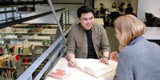 Zwei Studierende sitzen an einem Arbeitsplatz in der Bibliothek und lesen.